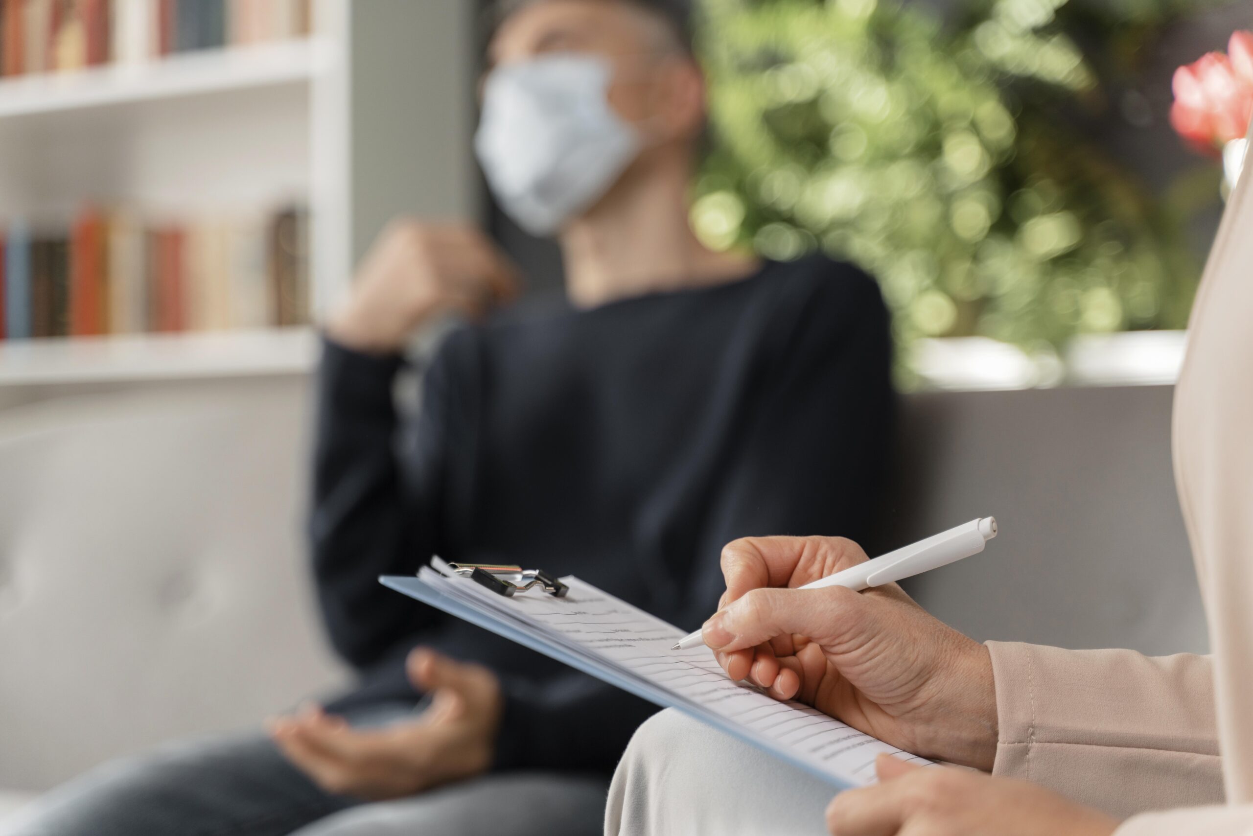 woman-therapist-taking-notes-of-man-in-therapy-office-with-mask